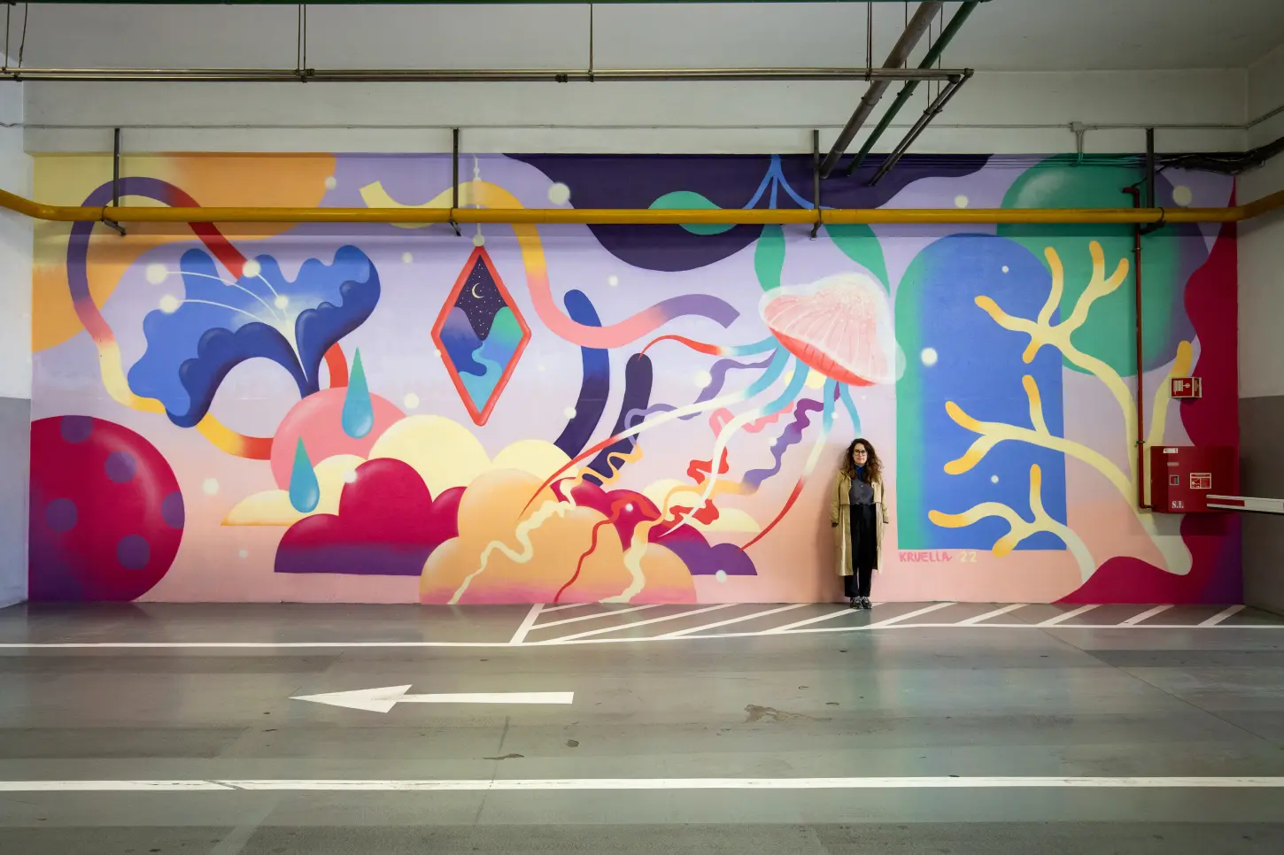 a woman standing in a parking lot with a colorful wall